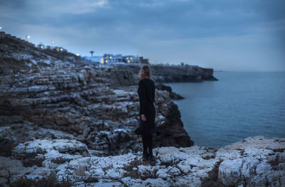 Rear view of woman standing on shore against sky