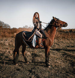 Full length of young woman riding horse on field