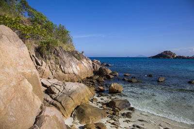 Scenic view of rocks on beach against blue sky