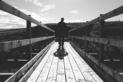 Rear view of woman standing on footbridge against sky