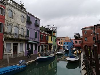 Boats moored in canal by buildings against sky