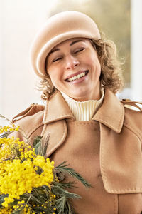 A young woman in a beige coat and hat with a bouquet of mimosa. international women's day