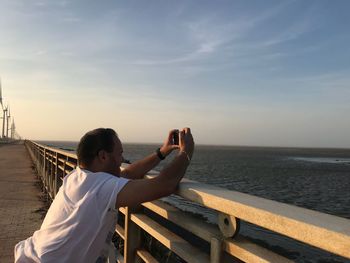 Man photographing sea against sky during sunset