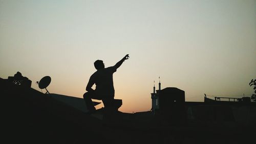 Rear view of man pointing towards sky while standing on rooftop during sunset