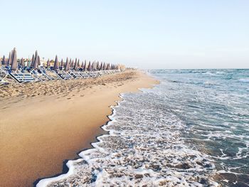 Lounge chairs and umbrellas at beach by sea against clear sky on sunny day