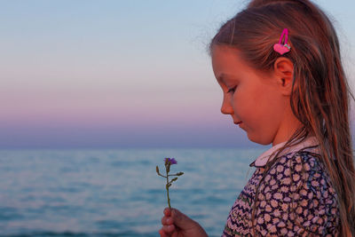 Adorable little girl looks on flower on beach.cute child with wet long hair in dress smelling flower