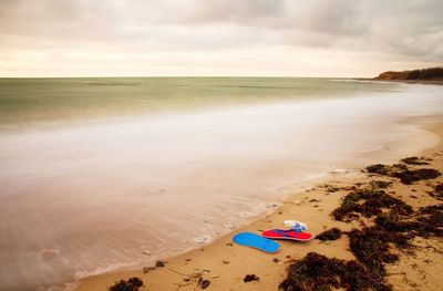 Blue red flip flops and white swimming goggles ready for using on stony beach at wooden breakwater