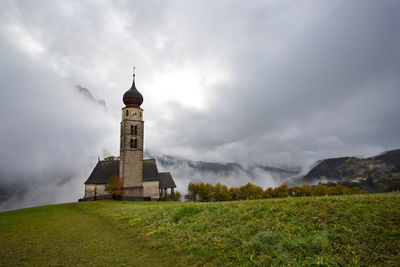 Lighthouse on field by building against sky