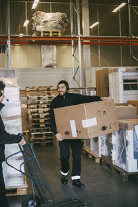 Male entrepreneur carrying box container at distribution warehouse