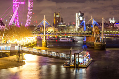 Illuminated bridge over river in city at night