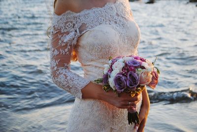 Close-up of bride holding flowers  while standing on beach