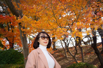 Portrait of young woman standing by tree during autumn