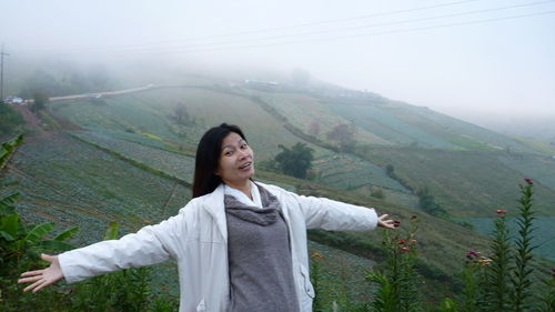 Portrait of smiling young woman against landscape during foggy weather