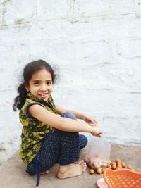 Side view portrait of smiling girl with food sitting by wall