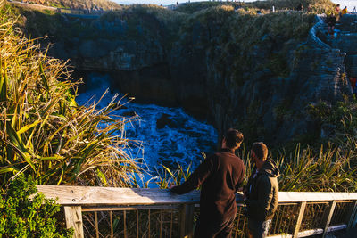 High angle view of friends talking while standing on footbridge over sea during sunset