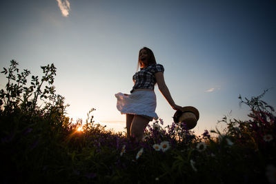Woman standing on field against sky during sunset