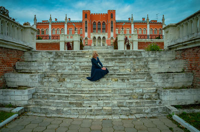 Woman sitting on staircase against buildings in city