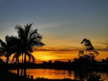 Silhouette palm trees by lake against sky during sunset