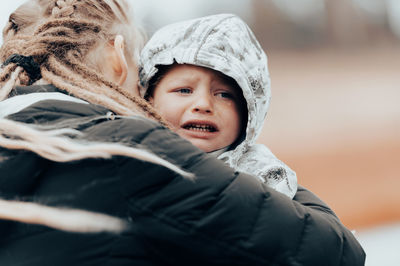 Mother holding crying baby, sad little boy being hugged by his mother