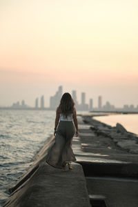 Rear view of woman standing by sea against sky during sunset