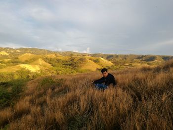 Man sitting on field against sky