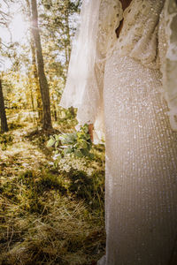 Midsection of mid adult bride wearing white wedding dress in forest