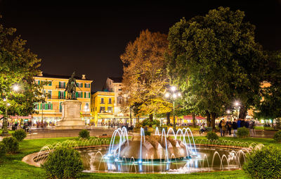 Illuminated fountain by pond in park at night