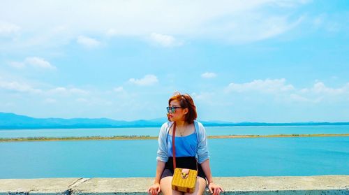 Woman sitting on wall by sea