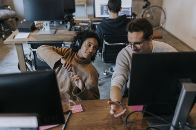 Smiling male hacker discussing with female colleague at desk in creative office