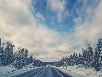 Road amidst snow covered landscape against sky