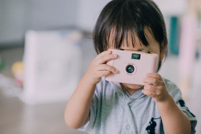 Portrait of girl holding camera while using mobile phone