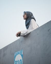 Low angle view of young man against wall against clear sky