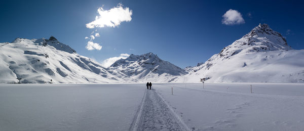 People walking on snow covered field against sky