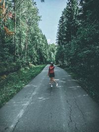 Rear view of woman walking on road amidst trees