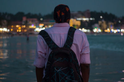 Rear view of man standing by river at night