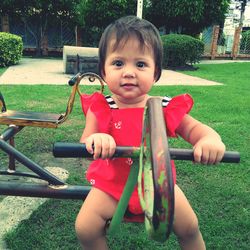 Portrait of baby girl sitting on play equipment at park