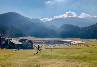 People on field by mountains against sky