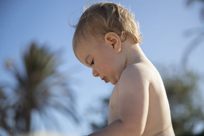 Side view of shirtless boy against sky