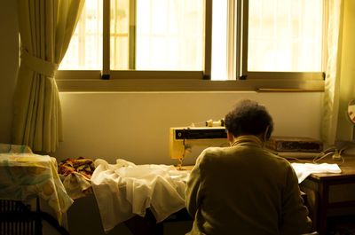 Rear view of man sewing clothes at home