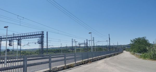 Road by electricity pylons against clear sky