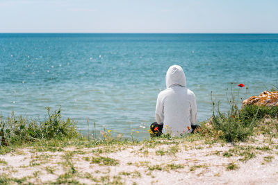 Rear view of man with white hood on beach against flowers and clear sky in summer