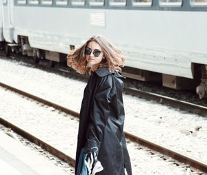 Side view of woman wearing sunglasses and black overcoat at railroad station platform