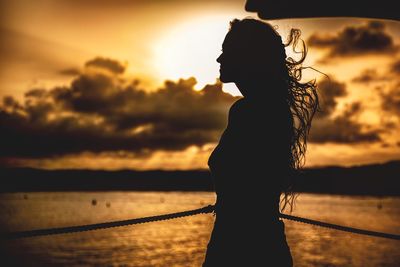 Silhouette woman standing by sea against sky during sunset