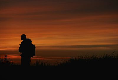 Silhouette of people standing on landscape at sunset