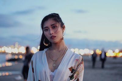 Portrait of young woman standing against sky at dusk