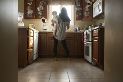 Rear view of mother with son standing in kitchen at home