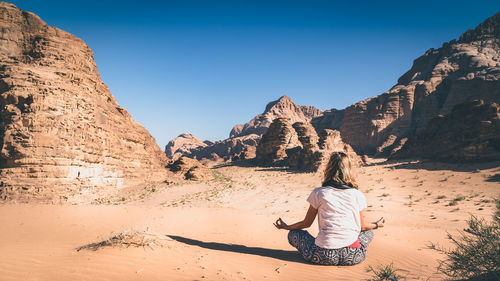 Rear view of woman meditating on field at desert