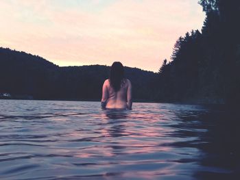 Rear view of naked young woman standing in lake during sunset