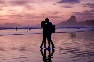 Couple on beach against sky during sunset