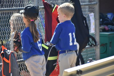 Boy and girl in sports jersey standing by chainlink fence